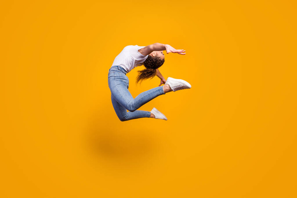 Full size profile photo of amazing lady flexible body bending spine artist dancer performance jumping high wear white t-shirt jeans isolated yellow bright color background - Foto, imagen