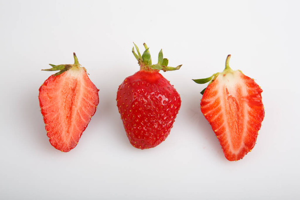isolated close up side view shot of a row of three whole and sliced in half vibrant red strawberries on a white background - Φωτογραφία, εικόνα