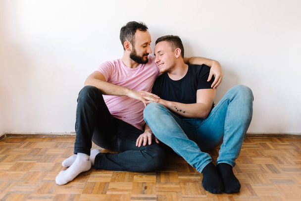 Stock photo of two caucasian homosexual men kissing in their apartment. One of them is hugging the other one from behind. - Photo, Image