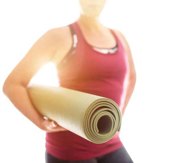 Young Woman holding rolled rubber gymnastic yoga mat on the white background light starting morning yoga exercises. Healthy and active people lifestyle concept. - Foto, Bild