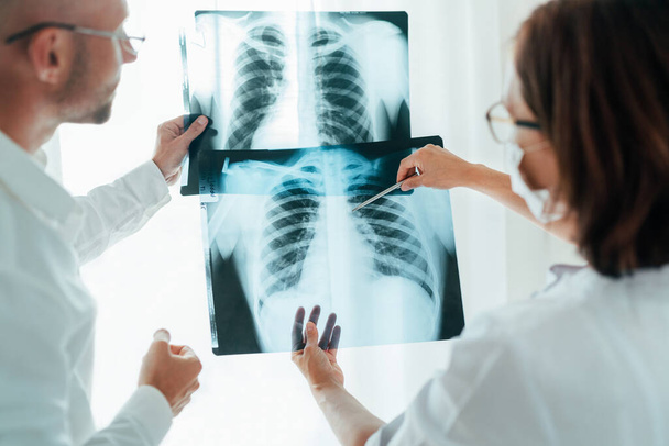 Male doctor and young female colleague examining patient chest x-ray film lungs scan at radiology department in hospital. Covid-19 xray test, covid worldwide virus epidemic spreading concept image. - Foto, Imagen