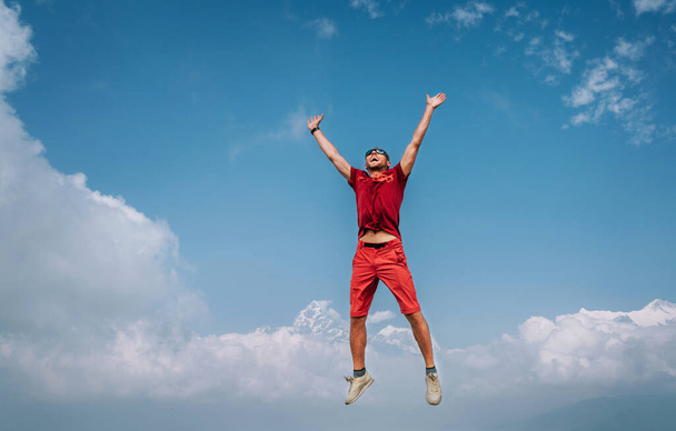 Happy man dressed red jumping over the clouds with Annapurna range mountains and Machapuchare 6993m mountain on background as he had trekking to Shanti (Peace) Stupa in Pokhara, Nepal. - Photo, image