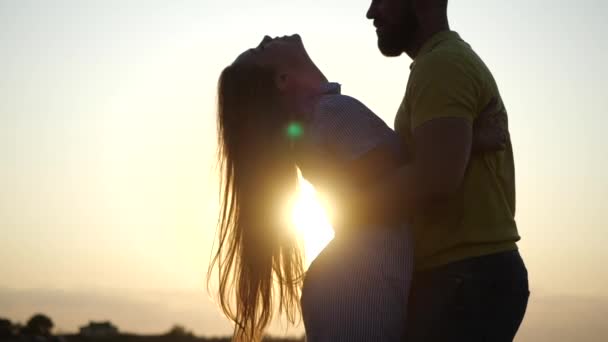 Liebendes junges Paar genießt Romantik und liebevolle Küsse in der Natur. Der bärtige Typ beugt sich über das schöne Mädchen mit den langen Haaren im Feld, Kulisse eines wunderbaren Sonnenuntergangs, Nahaufnahme in Zeitlupe. Termin im Freien - Filmmaterial, Video