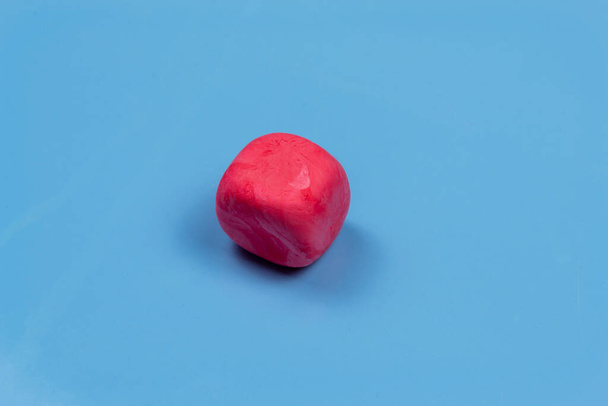 The pink cube is made of plasticine. On a blue background - Foto, Imagen