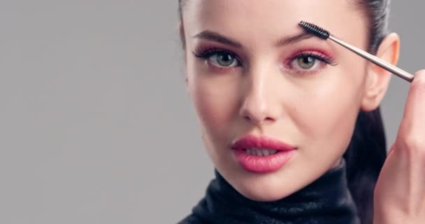 Young woman paints her eyebrows with an eyelash brush.  Cosmetic concept. Beautiful brunette model doing make-up. Woman makes makeup. 4k Slow motion footage. Closeup view. - Séquence, vidéo