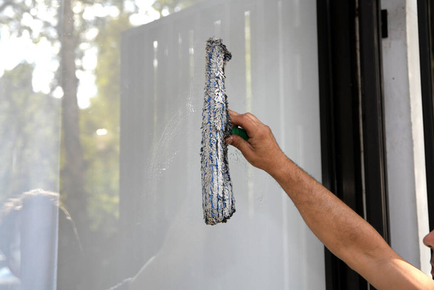 Fenster putzen. Ein junger Mann putzt und poliert Fenster mit einem Schwamm - Foto, Bild