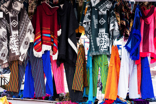 Традиционные пончо в разных цветах представлены на ремесленном рынке Отавало в Эквадоре
. - Фото, изображение