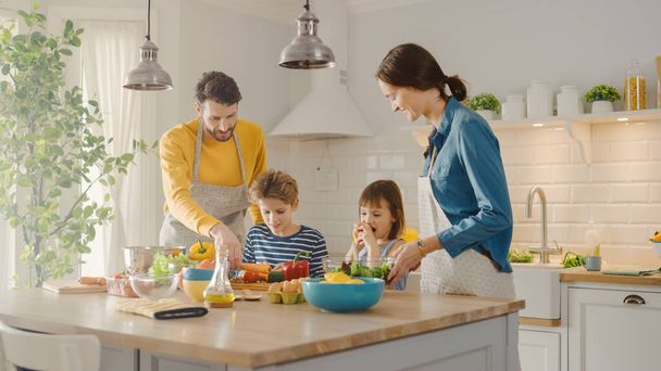 V kuchyni: Rodina čtyř vaření spolu zdravé večeře. Matka, otec, chlapec a dívka, příprava salátů, mytí a krájení zeleniny. Roztomilé děti pomáhají svým krásným starostlivým rodičům - Fotografie, Obrázek