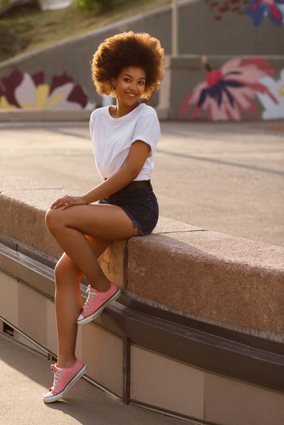 Dark-skinned girl smiles and sits in the city in the summer - Fotoğraf, Görsel