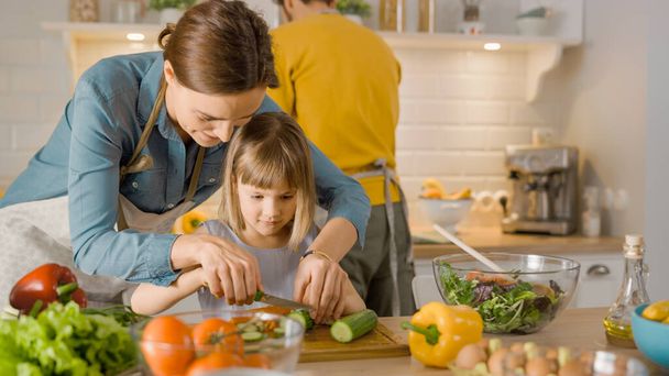 A konyhában: anya és aranyos kis lánya főzés együtt egészséges vacsora. Anya egészséges szokásokat tanít a kislánynak, és azt, hogyan vágja le a zöldségeket a salátához. Aranyos gyermek segít neki gyönyörű gondoskodó szülők - Fotó, kép