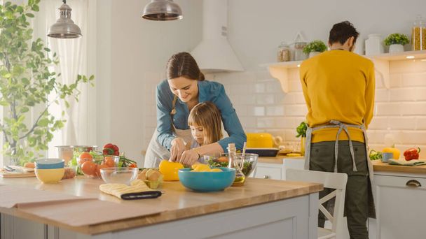 In Kitchen: Mother and Cute Little Daughter Cooking Together Healthy Dinner. Mom Teaches Little Girl Healthy Habits and how to Cut Vegetables for Salad. Cute Child Helping Her Beautiful Caring Parents - Foto, imagen