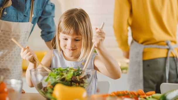 In Kitchen: Mother and Little Daughter Cooking Together Healthy Dinner. Mom Teaches Little Girl Healthy Habits and how to Mix Vegetables in Salad Bowl. Cute Child Helping Her Beautiful Caring Parents - Фото, зображення