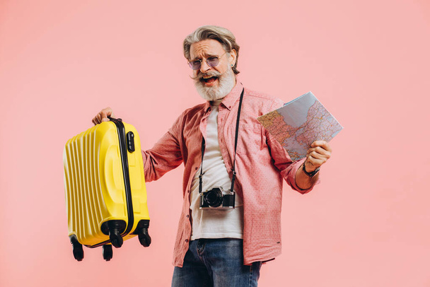 Happy bearded man in sunglasses holds a suitcase and a map, sings and dances - Photo, Image