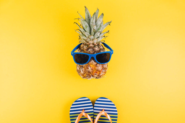 Zomer concept. Leuke en grappige ananas met zonnebril en teenslippers op gele achtergrond.  - Foto, afbeelding