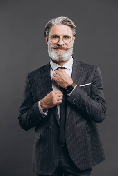 Portrait of a business and fashionable mature man in a gray suit straightens his tie - Foto, afbeelding