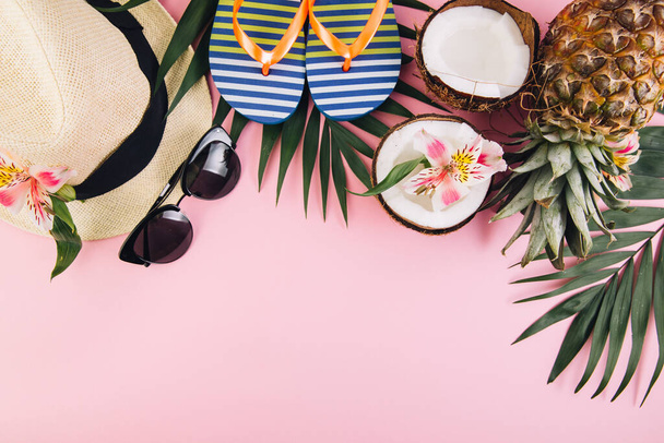 Tropical palm leaves, hat, slippers, sunglasses, pineapple, coconut on pink background. Summer concept. Flat lay, top view, copy space - Photo, Image