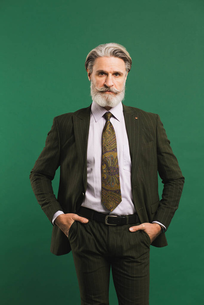 Стильный бородатый мужчина средних лет в костюме хаки на зеленом фоне
 - Фото, изображение