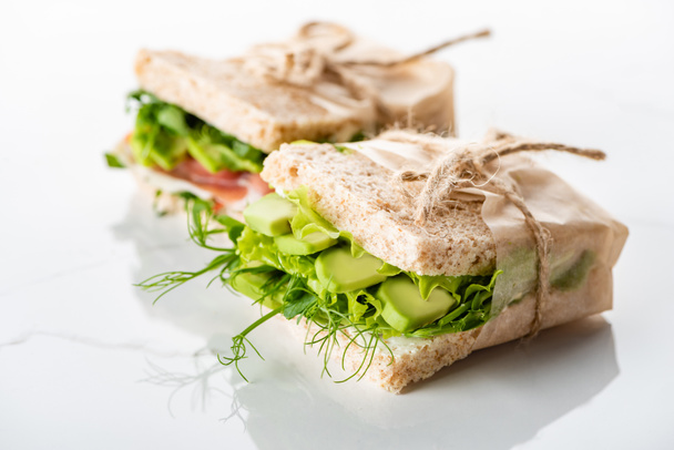 selective focus of fresh green sandwiches with avocado on marble white surface - Foto, afbeelding
