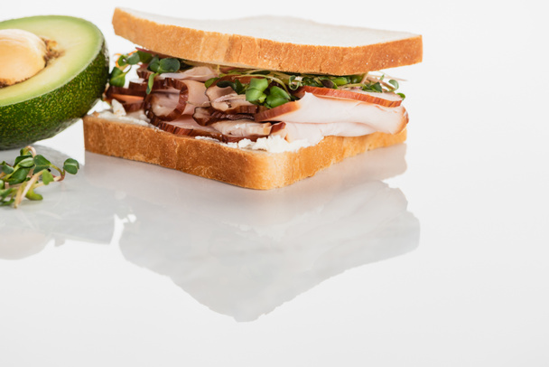 verse heerlijke sandwich met vlees en spruiten op wit oppervlak in de buurt van avocado - Foto, afbeelding