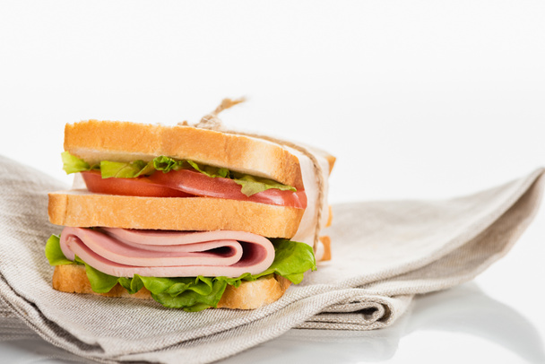 delicioso sándwich fresco con salchicha en rodajas y lechuga en la servilleta en la superficie blanca
 - Foto, Imagen