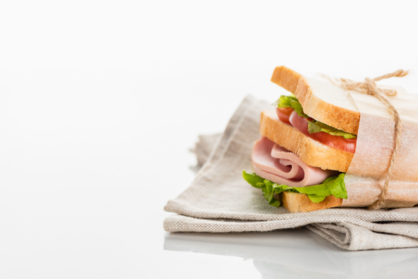 fresh delicious sandwich with sliced sausage and lettuce on napkin on white surface - Фото, изображение