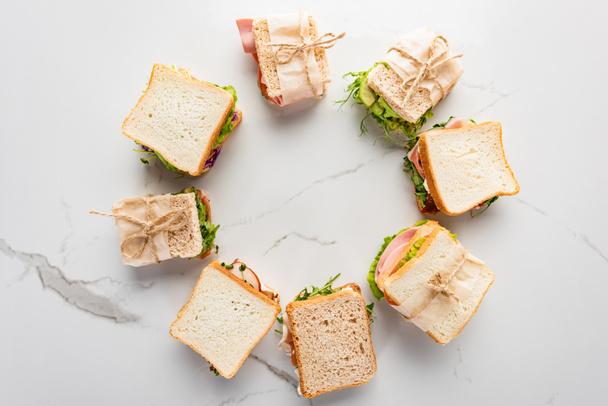 top view of fresh sandwiches arranged in round frame on marble white surface - Photo, image