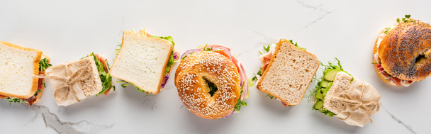 flache Lage mit frischen Sandwiches und Bagels auf marmorweißer Oberfläche, Panoramaaufnahme - Foto, Bild
