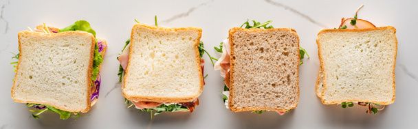 bovenaanzicht van verse sandwiches op marmeren wit oppervlak, panoramisch schot - Foto, afbeelding
