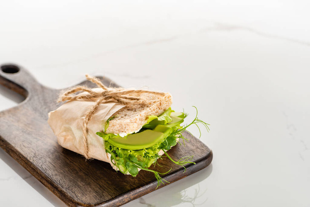 fresh green vegan sandwich with avocado on wooden cutting board on white marble surface - Φωτογραφία, εικόνα