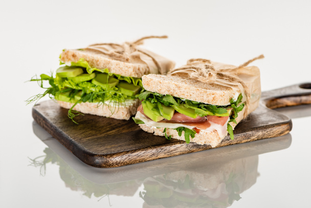 Avokadolu taze yeşil sandviçler ve beyaz yüzeydeki tahta kesme tahtasının üzerinde et. - Fotoğraf, Görsel