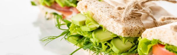 foco seletivo de sanduíche verde fresco com abacate na superfície branca, tiro panorâmico
 - Foto, Imagem