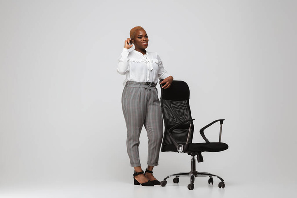 Jonge Afrikaans-Amerikaanse vrouw in kantoor kledij op grijze achtergrond. Lichaamspositief vrouwelijk karakter. plus grootte zakenvrouw - Foto, afbeelding
