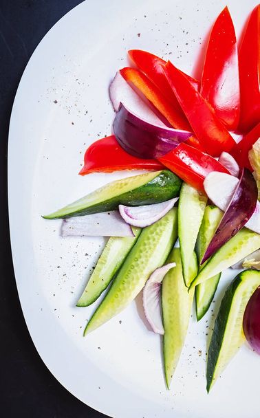 Fresh vegetarian salad in flat lay.Natural raw food served on plate in restaurant.Healthy keto diet meal cooked with natural ingredients:sweet red peppers,green cucumbers,red onions - Foto, Bild