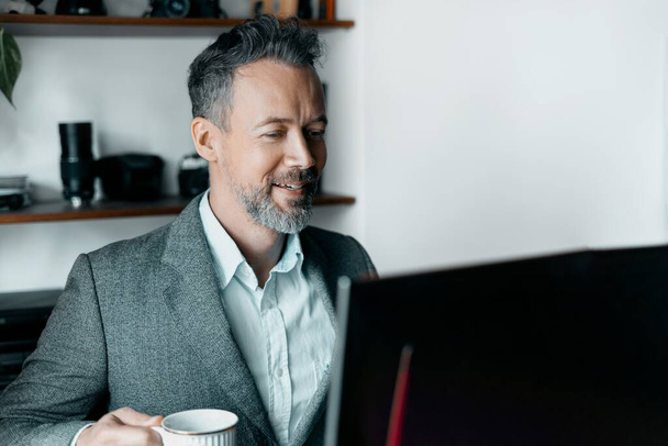 Hombre feliz con taza de café usando el ordenador portátil en casa
 - Foto, imagen