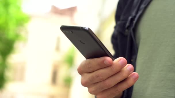 Close-up van de hand van een blanke jonge man met een telefoon. Een man typt een bericht op straat. - Video