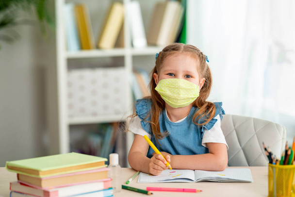 little girl is sitting at table, doing homework at home. child smiles happily and gets knowledge during quarantine period. digital concept e-learning, during epidemic, self-isolation. Back to school. - 写真・画像