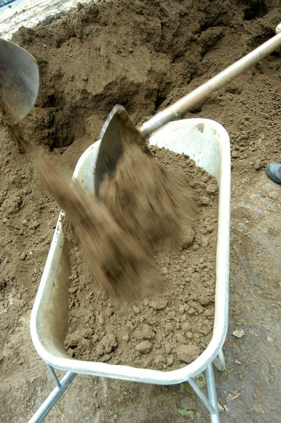 shovel filling a wheelbarrow with sand at the construction site - Photo, Image
