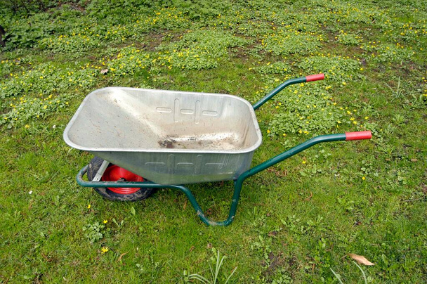 empty wheelbarrow with red handles on a green meadow with yellow flowers - Photo, Image
