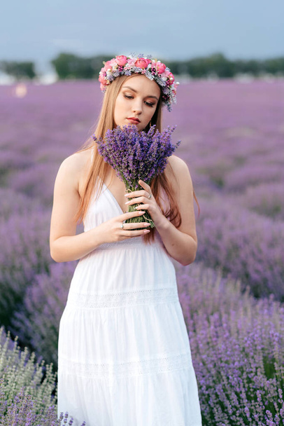 Young dreamy woman with bouquet in her hands standing in flowering lavender field, close up - Foto, Imagem