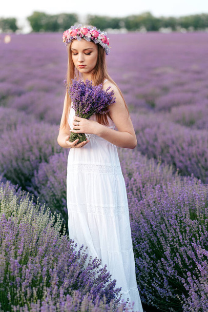 Молодая мечтательная женщина с букетом в руках стоит на цветущем лавандовом поле, крупным планом
 - Фото, изображение