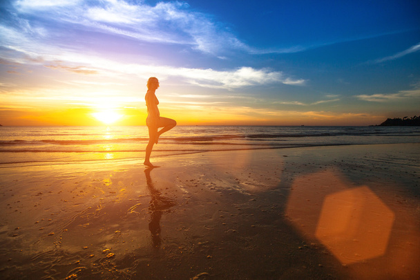 silhouet van een jonge vrouw doen oefeningen bij zonsondergang op de kust. - Foto, afbeelding