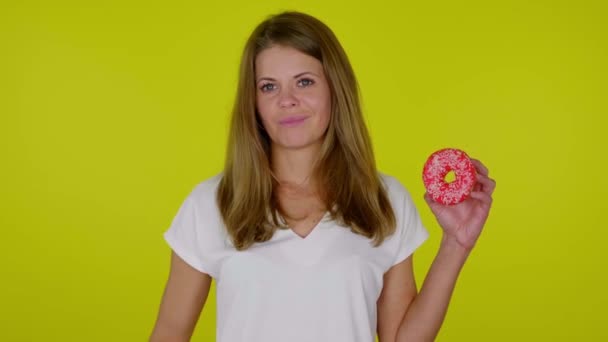 Woman raises hand with a red donut, shows dislike, grimaces on yellow background - Footage, Video