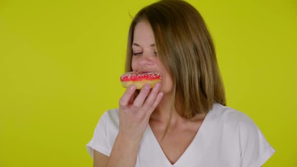 Donna in una maglietta bianca morde, mangia un insapore ciambelle rosse, sconvolto con gusto - Filmati, video
