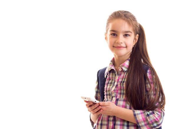 Positive schoolgirl looking in camera while holding smartphone - Фото, изображение