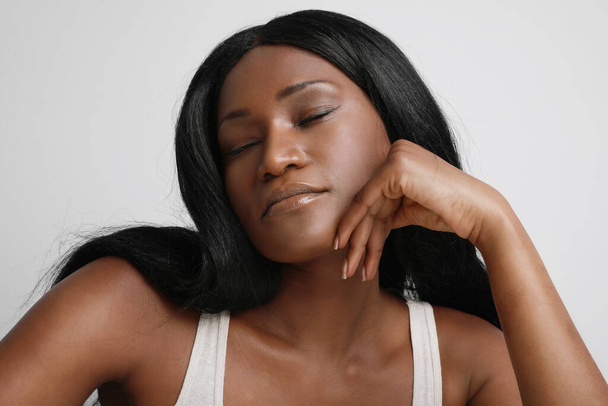 Studio shot of beautiful black woman, with closed eyes, posing over white wall.Skin care concept. - Photo, image