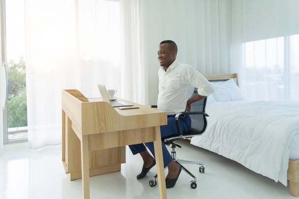 Fáradt üzleti fekete amerikai férfi, afrikai ember szenved hátfájás vagy görcs, dolgozik a számítógép notebook laptop és ül a széken hosszú ideig. Hátfájás. Fáj az izom. Office-szindróma. - Fotó, kép