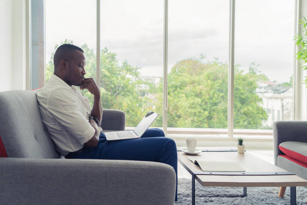 Üzleti fekete amerikai férfi, afrikai személy dolgozik otthonról, gondolkodás probléma a számítógép notebook laptop és szenved a depresszió karanténban a corona vírus világjárvány koncepció. - Fotó, kép