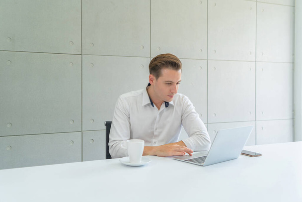 Portret van een glimlachende zakelijke blonde, blanke man, blanke persoon die online werkt in kantoor in de vergaderruimte in technologie apparaat concept. Levensstijl. - Foto, afbeelding