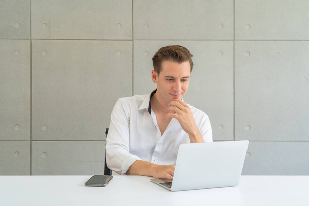 Portret van een glimlachende zakelijke blonde, blanke man, blanke persoon die online werkt in kantoor in de vergaderruimte in technologie apparaat concept. Levensstijl. - Foto, afbeelding