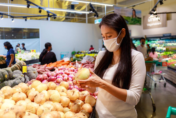 保護顔マスクを身に着けているアジアの女性は、スーパーマーケットのデパートでショッピングカートを押します。食料を買う食料品を探してる。covid-19の後の新しい通常。家族の概念. - 写真・画像